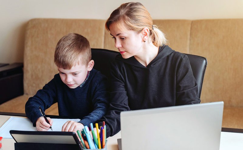 Eine Mutter unterstützt ihren Sohn während ihrer Homeoffice-Tätigkeit bei den Hausaufgaben.